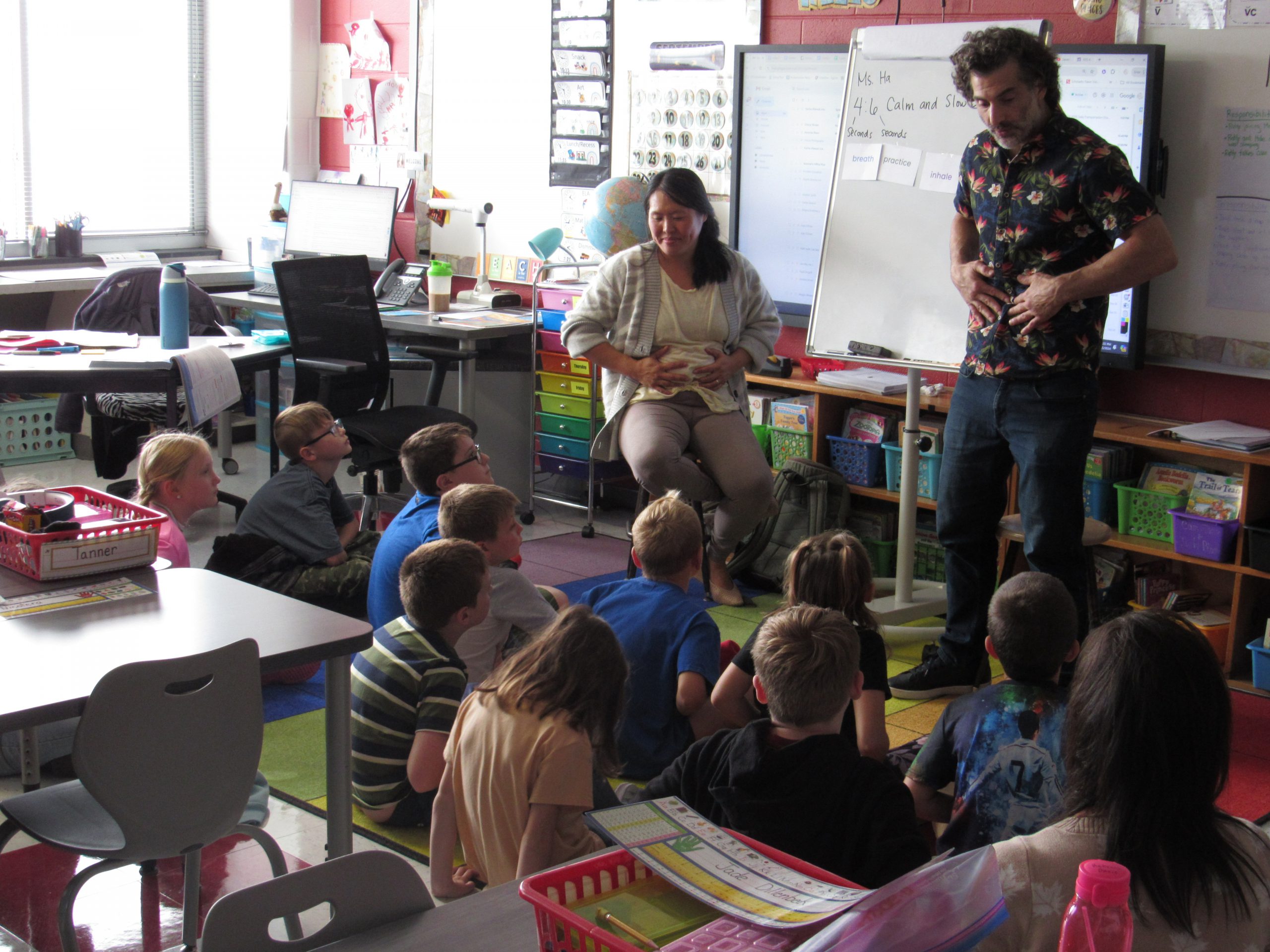 Kathy Ha, and Michael Christoforo from Terranuma Schools, teach a third grade classroom breathing techniques in front of the classroom, with of a group of kids sitting on the rug watching them.