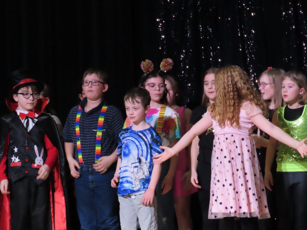 OESJ Students stand on stage in unity in their costumes after preforming in the talent show.